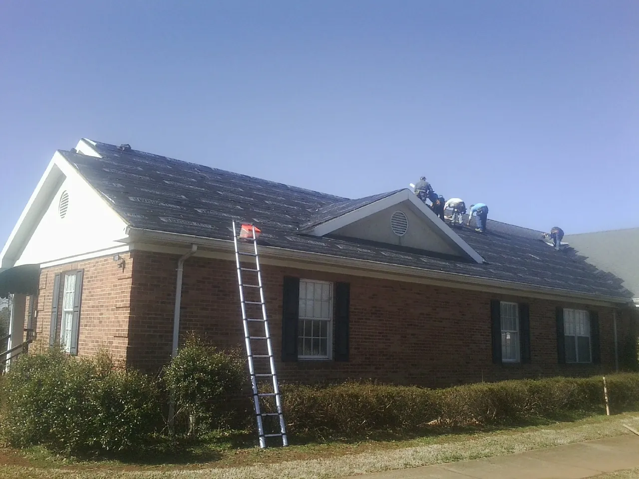 Crew tearing shingles off a brick ranch roof with a ladder set — Emergency Roof Repair work by our crew in Henning