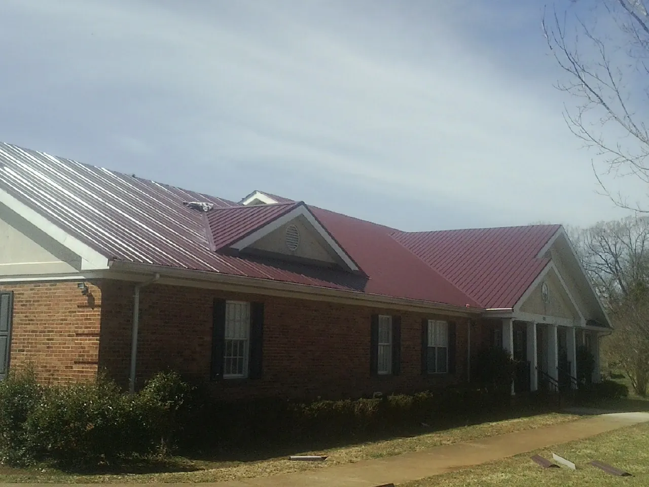 Red metal roof with gabled entries on a long brick building, from a Hail Damage Roof Repair job in Henning