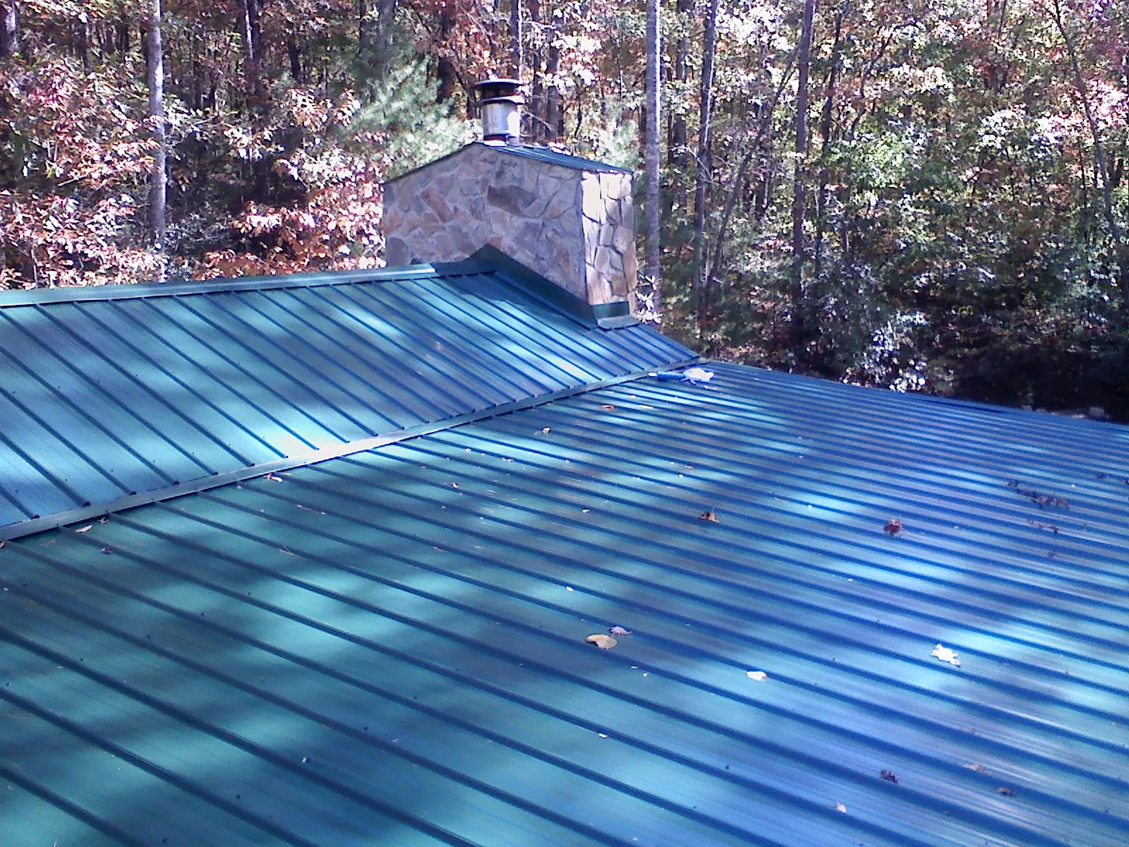 New green metal roof and stone chimney surrounded by autumn woods in Henning